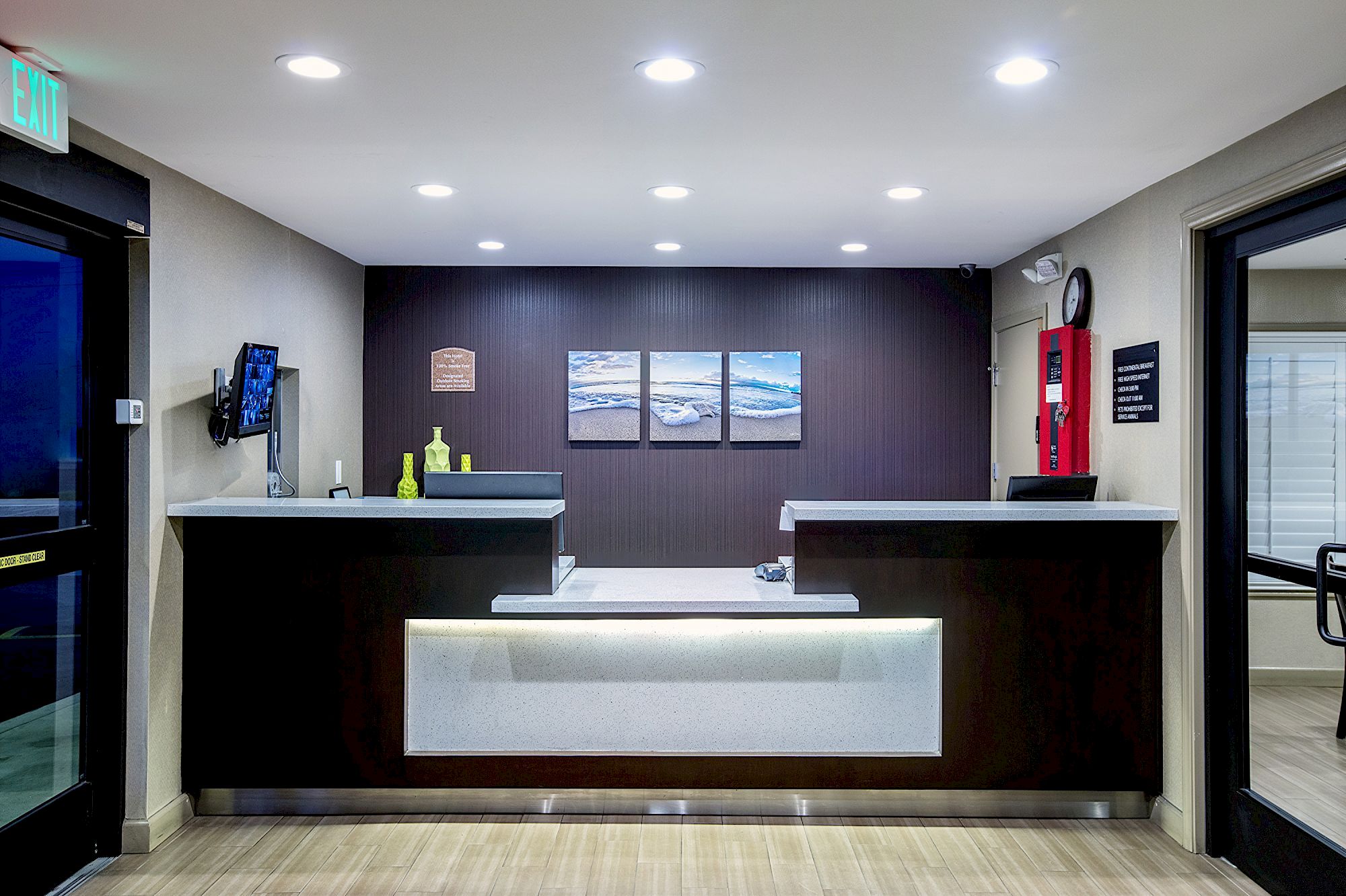 A modern reception desk area with a dark backdrop featuring three wall pictures, illuminated from above, and minimalistic decor.